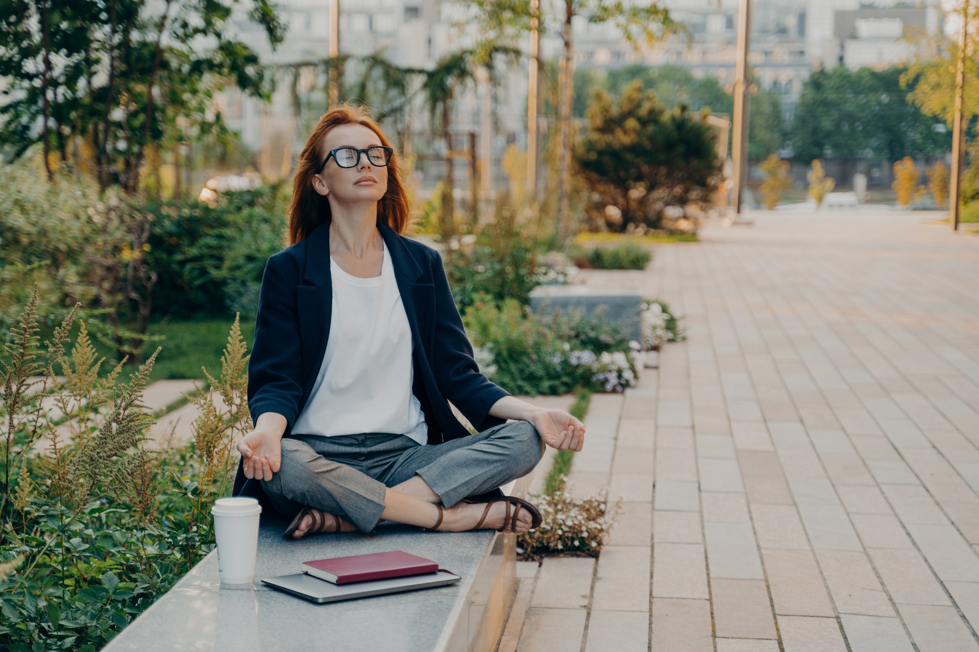 Calm business woman meditating in lotus outdoors, peaceful female freelance employee practicing yoga